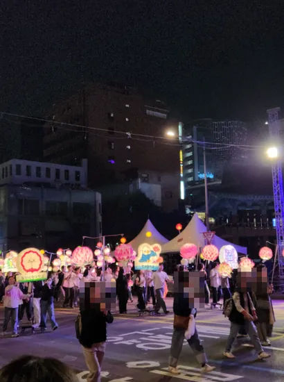 People walking together at night while carrying lanterns, taking part in a festive street procession.