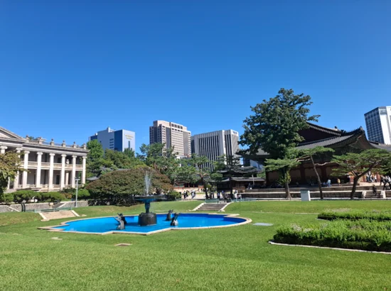 MMCA Deoksugung courtyard with a blue fountain pool, palace building, and downtown Seoul skyline on a clear day