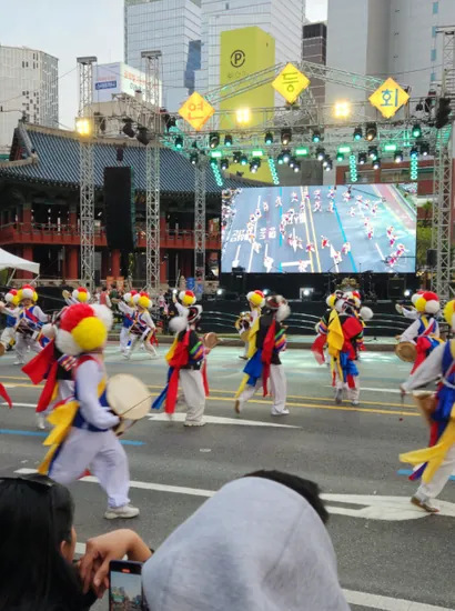 Samulnori performers playing traditional percussion during a lively street festival parade, entertaining the crowd.