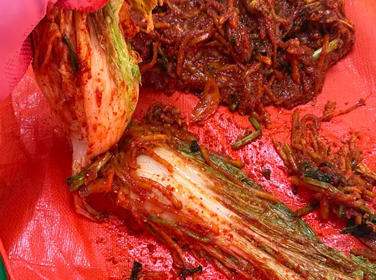 A close-up image showing a kimchi-making scene at a Seoul kimchi museum, with napa cabbage and seasoning spread during the preparation process.